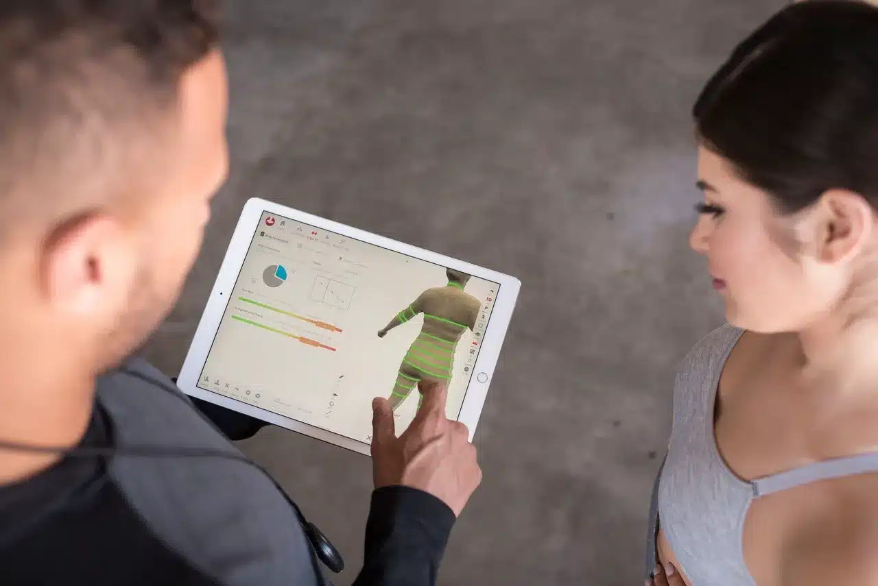 A person is using a tablet to analyze a 3D model of a figure, while another person observes.